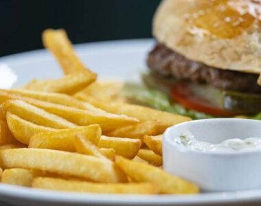 pomfrit, hamburger i dve činijice sa sosevima servirani na belom tanjiru